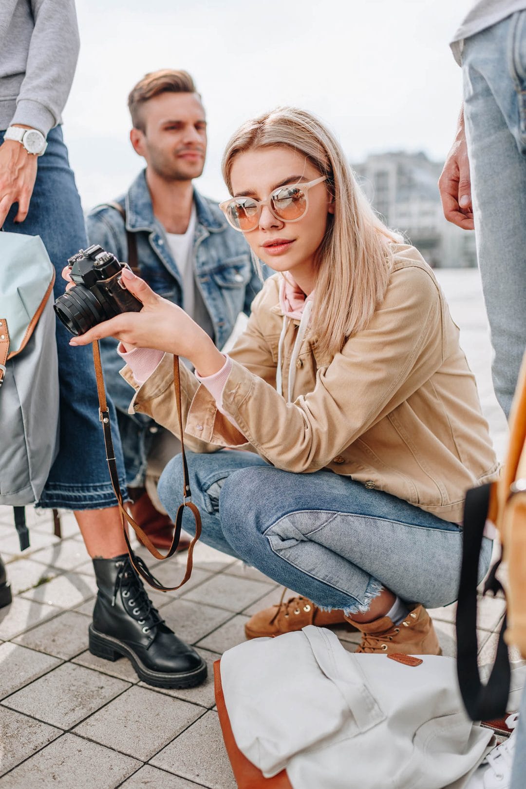 girl sunglasses crouched crowd camel jacket blonde hair blue jeans street photography portrait city people camera subject light how to tutorial guide
