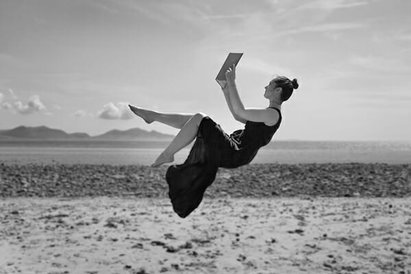 model floating on beach with a book in black and white