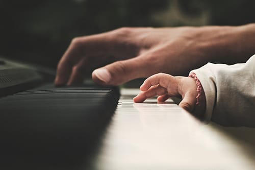 hand of a parent and baby playing the piano