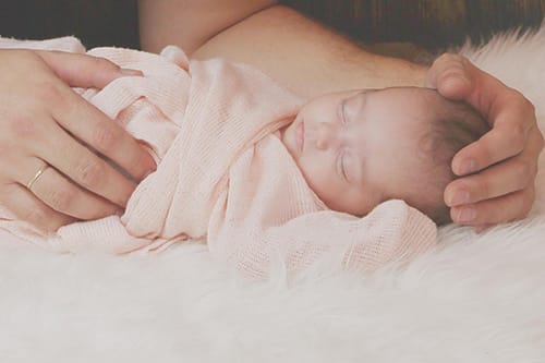 baby wrapped in pink blanket asleep soft light