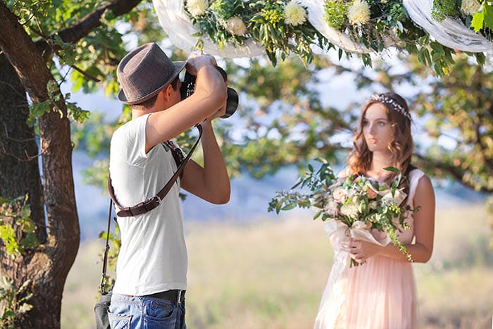 male wedding photographer wearing a hat taking a photo of a bridesmaid wearing pink dress