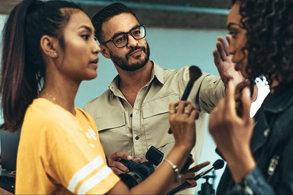 Makeup artist doing makeup to a model using a brush. Photographer talking to model about the photo shoot. working with models