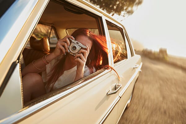 female leaning out of a car window taking a picture