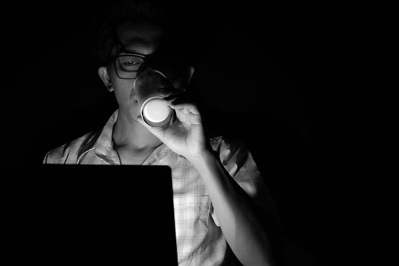 Low Light Portrait Man Drinking at a Laptop