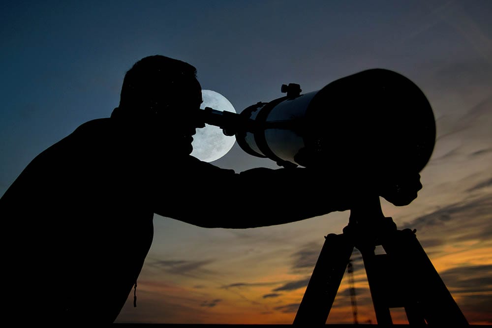 Adult man using a telescope at sunset time observing the moon at night. Amateur astronomy concept with empty copy space for Editor's