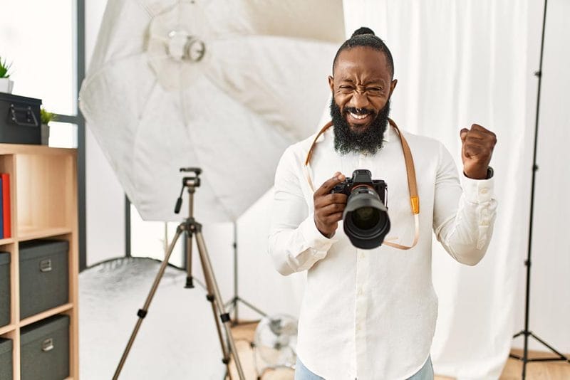African american photographer man working at photography studio very happy and excited doing winner gesture with arms raised, smiling and screaming for success. celebration concept.