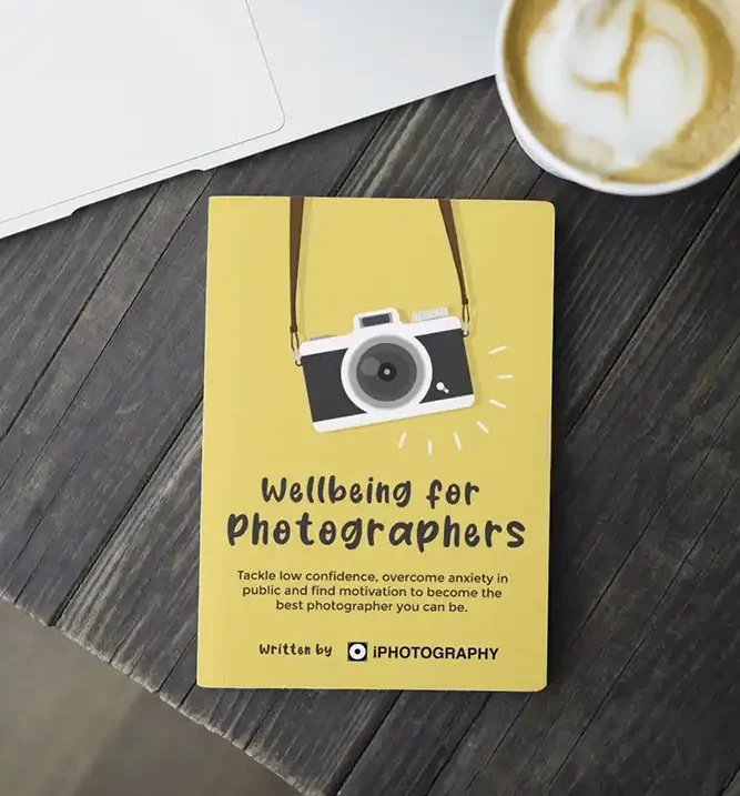a yellow book called wellbeing for photographers on a wooden table next to a coffee cup