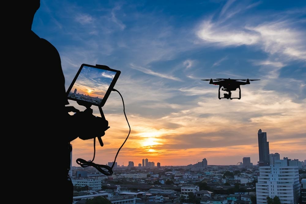 Man playing with the drone. Silhouette against the sunset sky over the city.