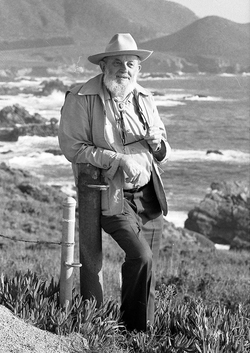 Ansel Adams wearing a hat leaning on a post