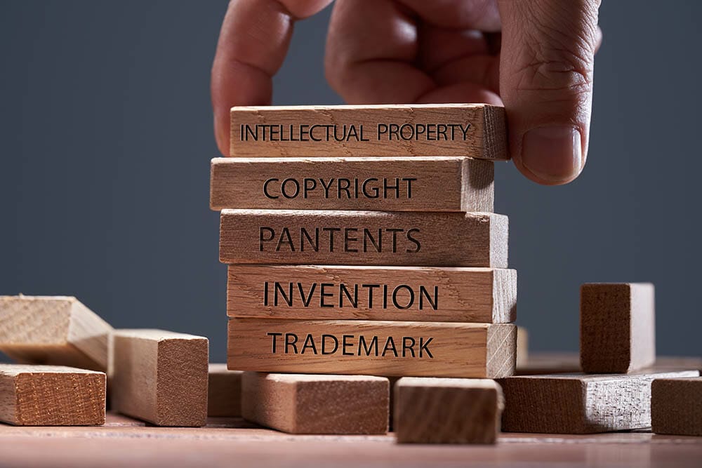 man adding a block showing the words ’Intellectual property’ on top of other wooden block with text copyright, patents, invention,and trademark