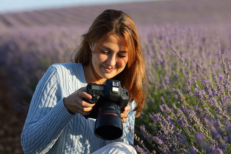 Happy photographer woman checking dslr camera in lavender field