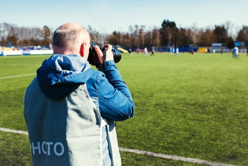 Photographer with professional tele-optics filming a football match at the stadium