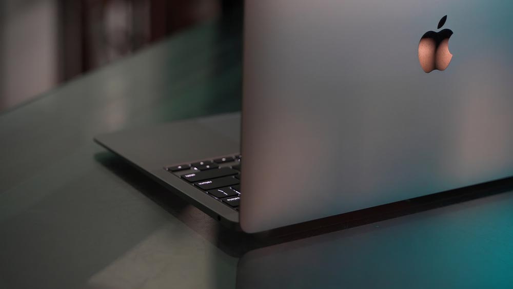 A shot of a space grey MacBook laptop's back with a logo on top of table