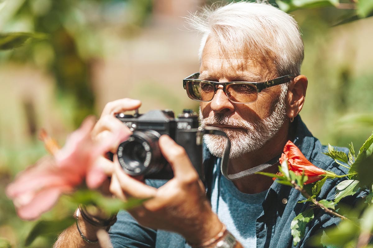 An elderly gray-haired man photographs a flower in the park, portrait.