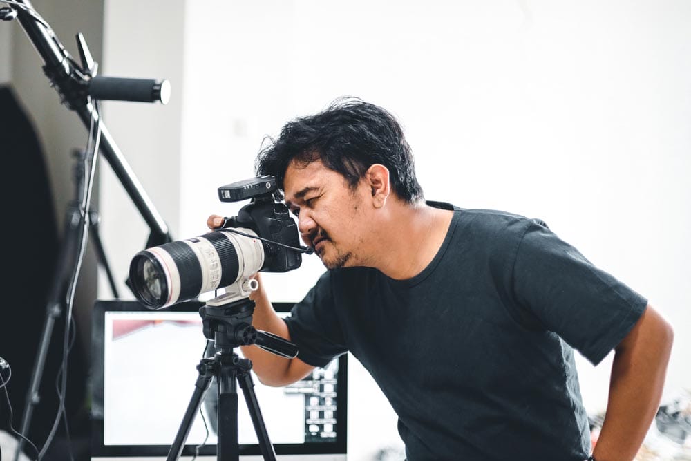 Male photographer taking pictures with his camera and tripod with a monitor and light stand in the background