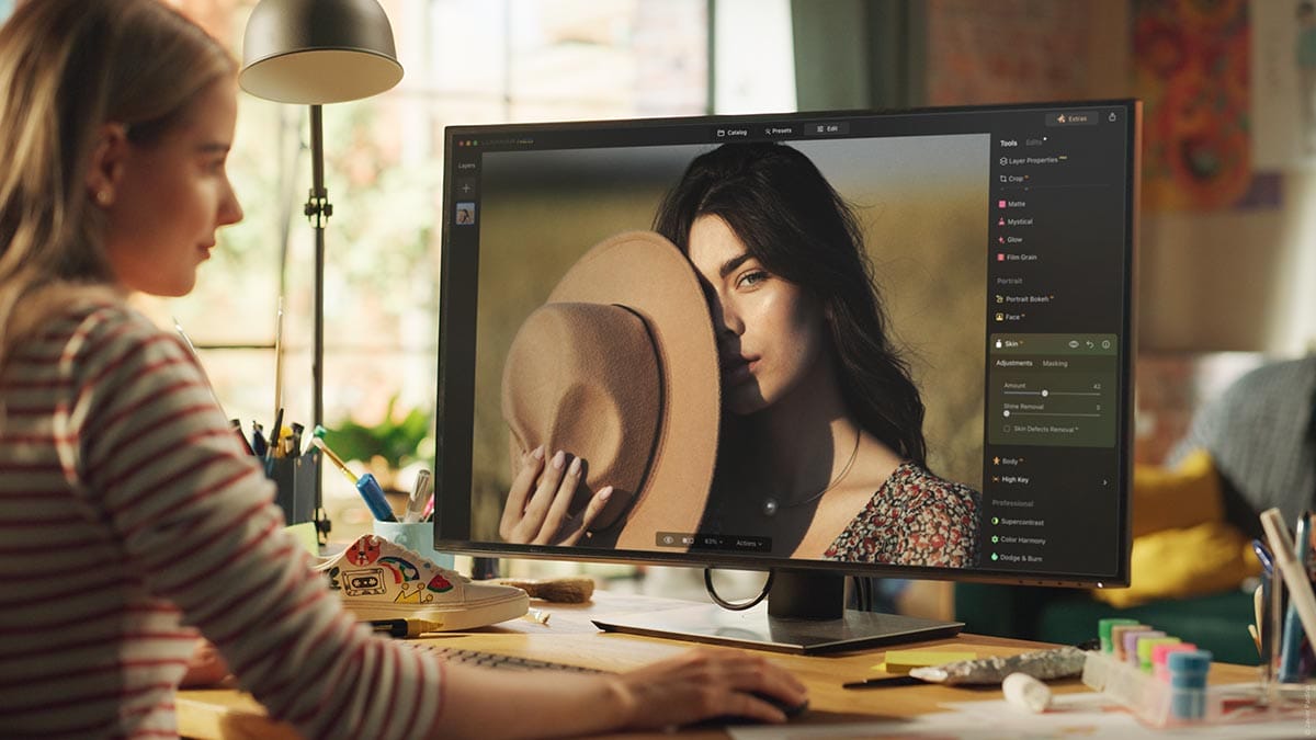 A lady sat at a PC editing a portrait photo on luminar neo