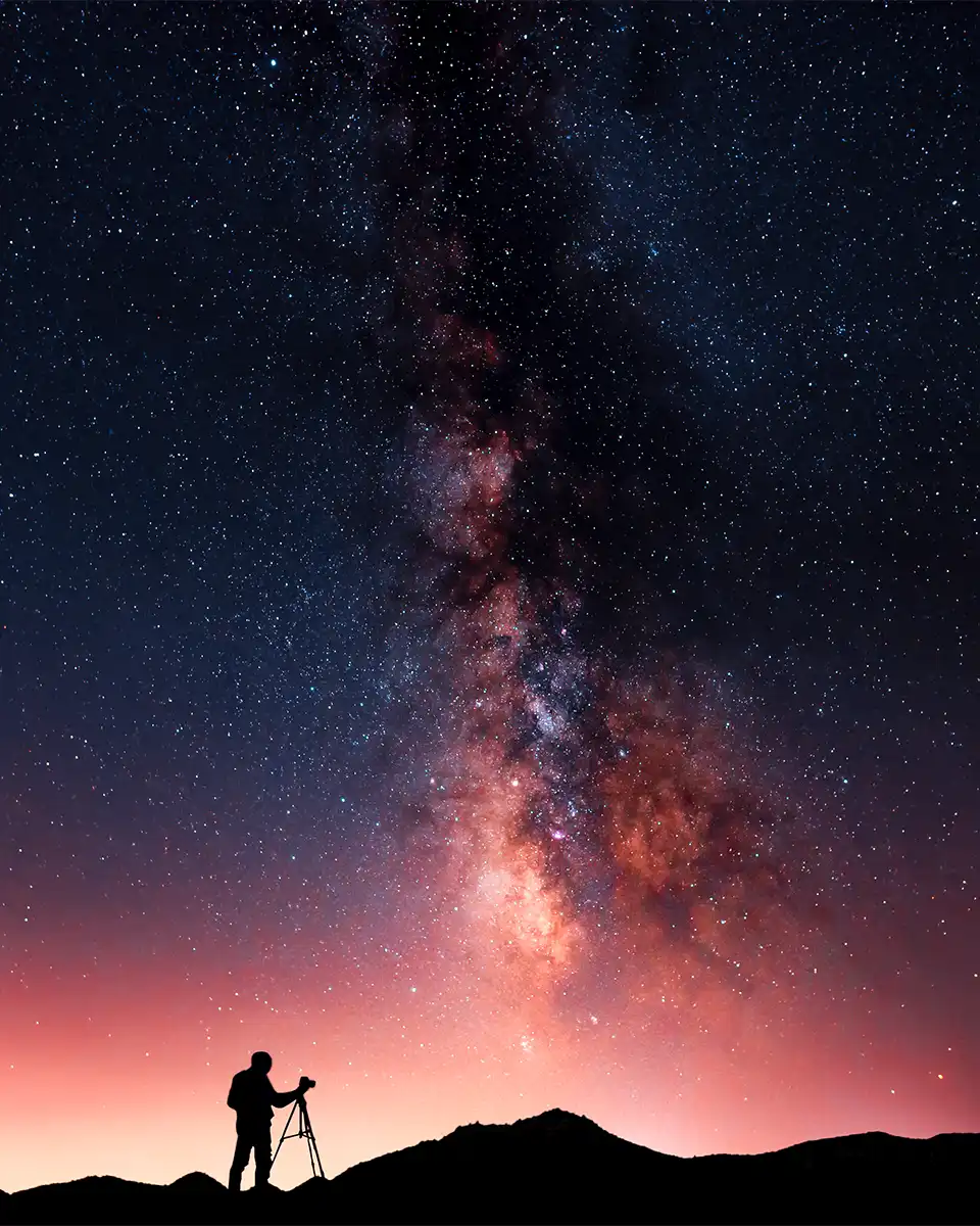 a silhouette of a photographer with a camera looking up at the milky way stars