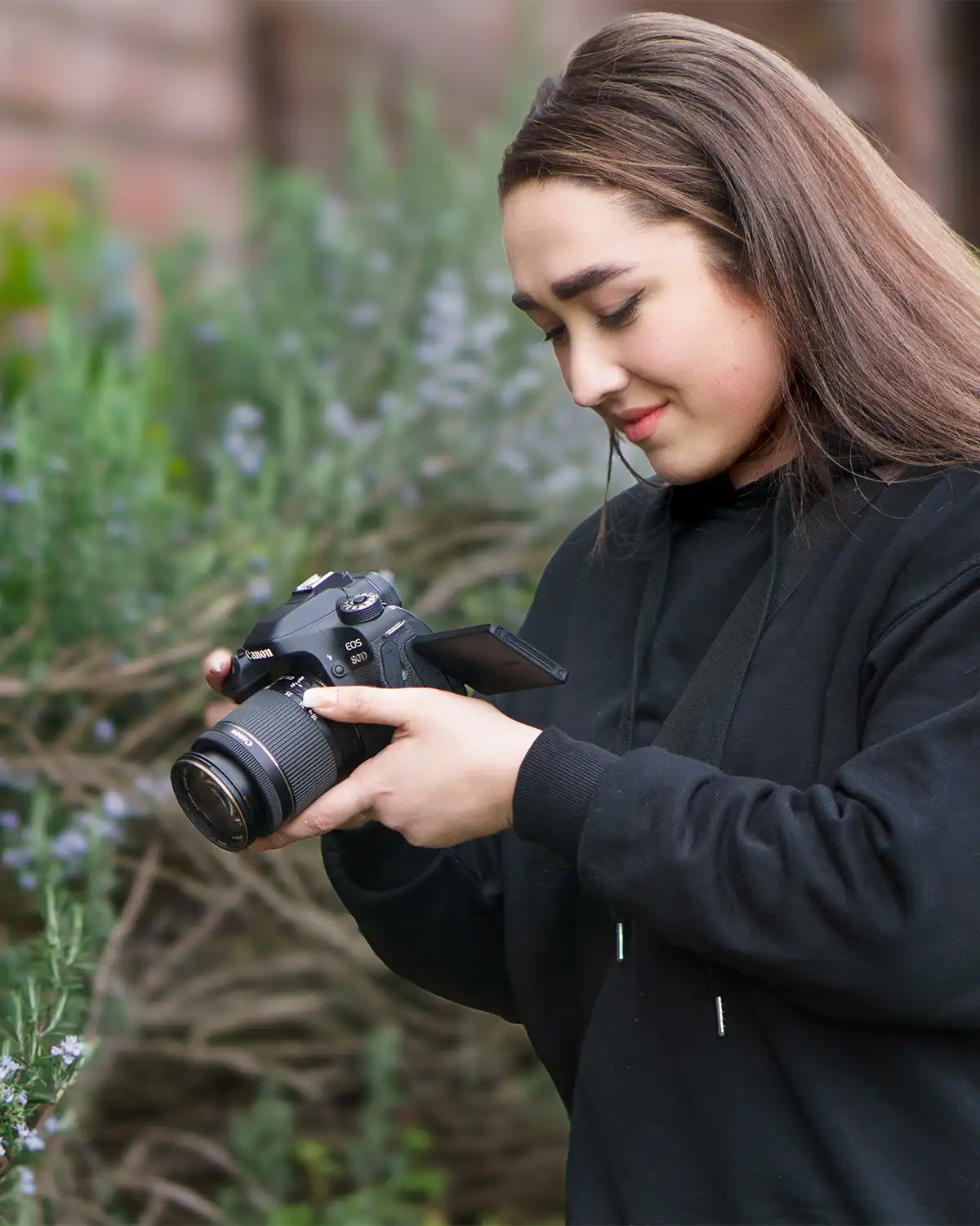 a female photographer with a digital camera taking photos of plants in a garden wearing a black hoodie jumper