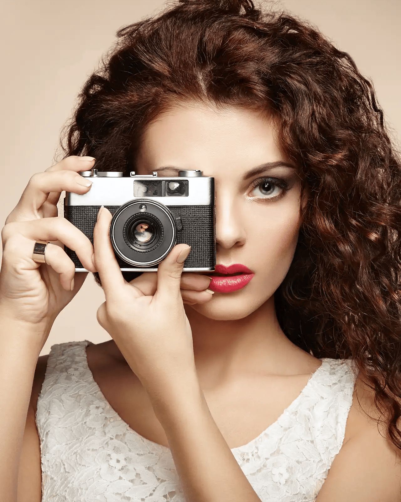 a lady with brown frizzy hair holding a vintage film camera taking a photo