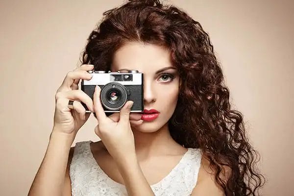 a lady with brown frizzy hair holding a vintage film camera taking a photo