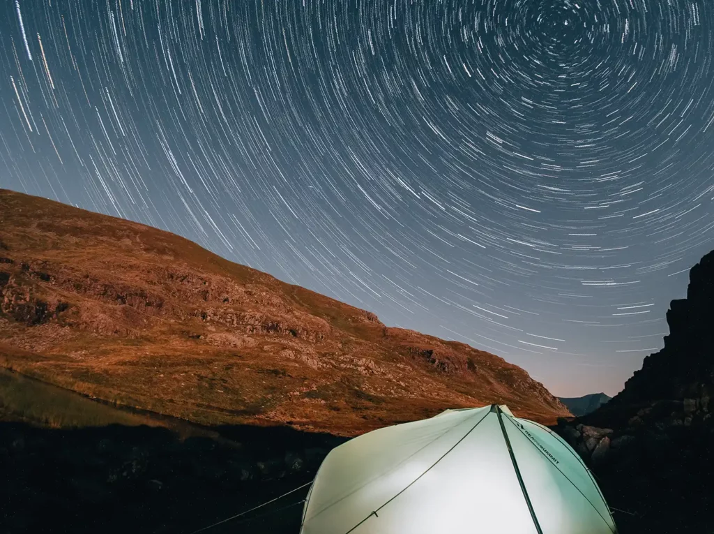 star trails in the sky with a lit up tent on the ground