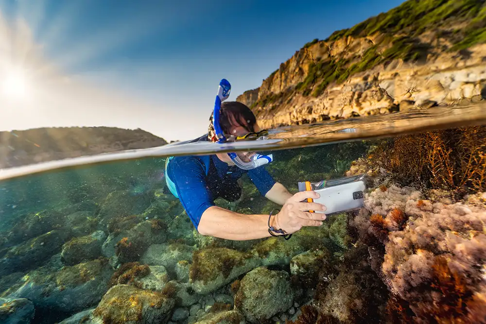 A photo of a man taking a photo underwater using a mobile phone in an underwater case