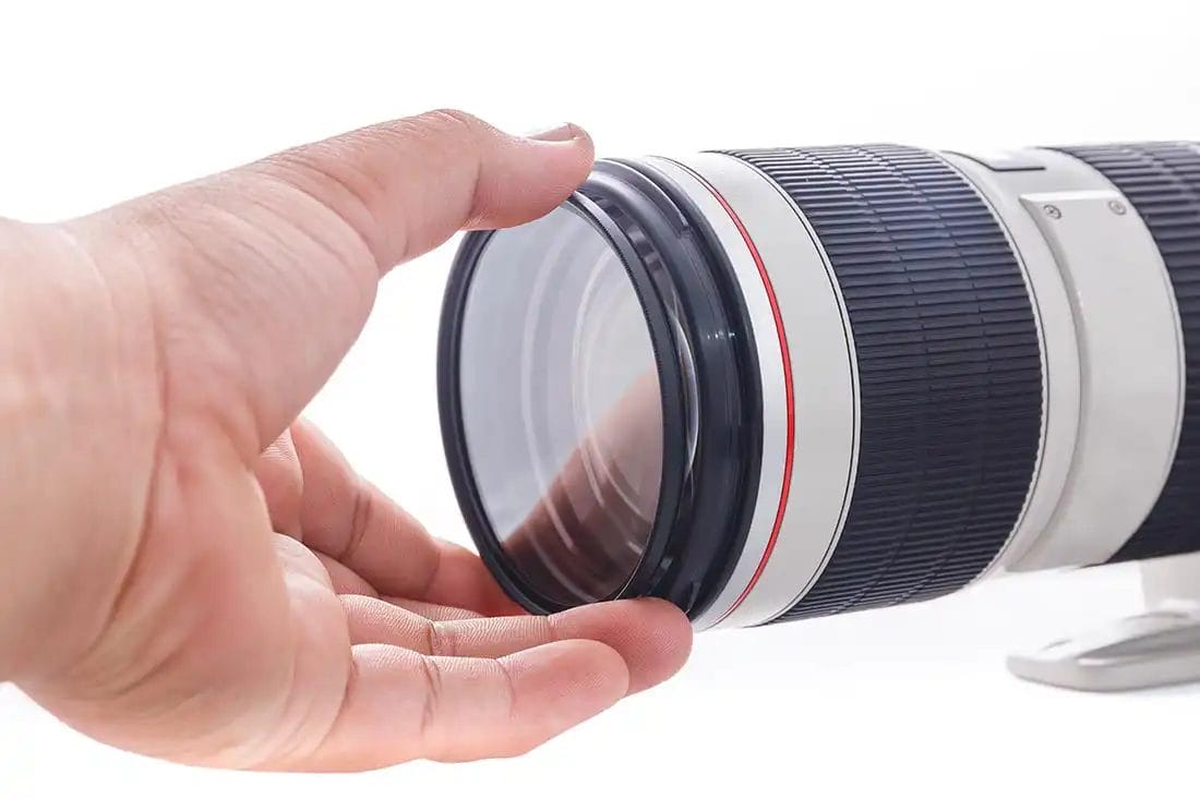 a hand twisting on a lens filter onto a camera lens