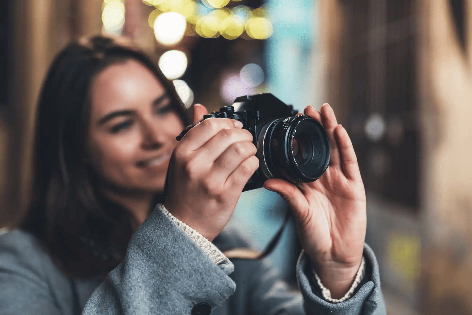 A smiling lady looking through the back of a camera adjusting the focus with her left hand