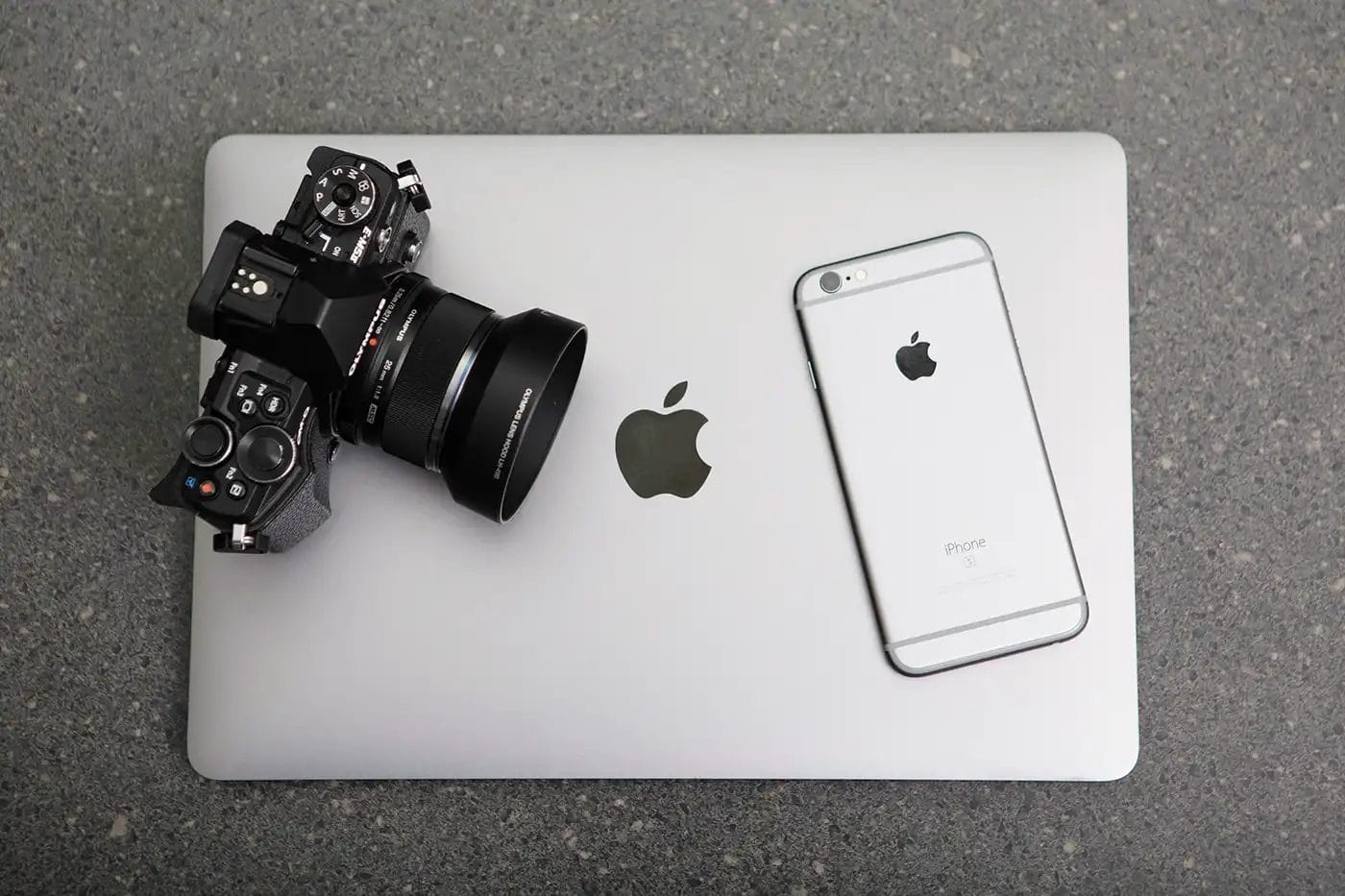 a digital camera next to an iphone facing down on top of an apple mac laptop