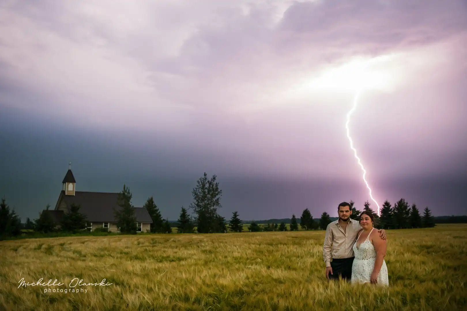A couple stood in a field with a lighting strike behind them