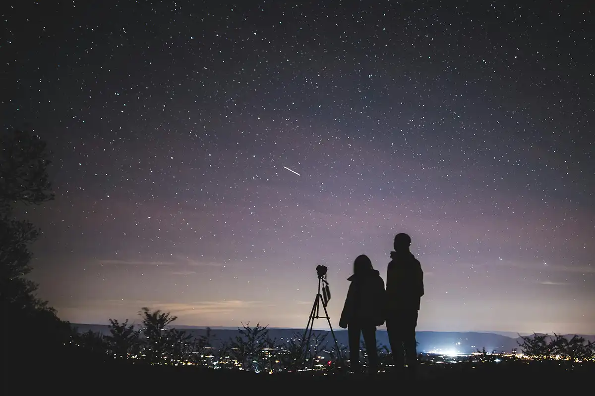 two people stood next to a camera at night looking at the stars